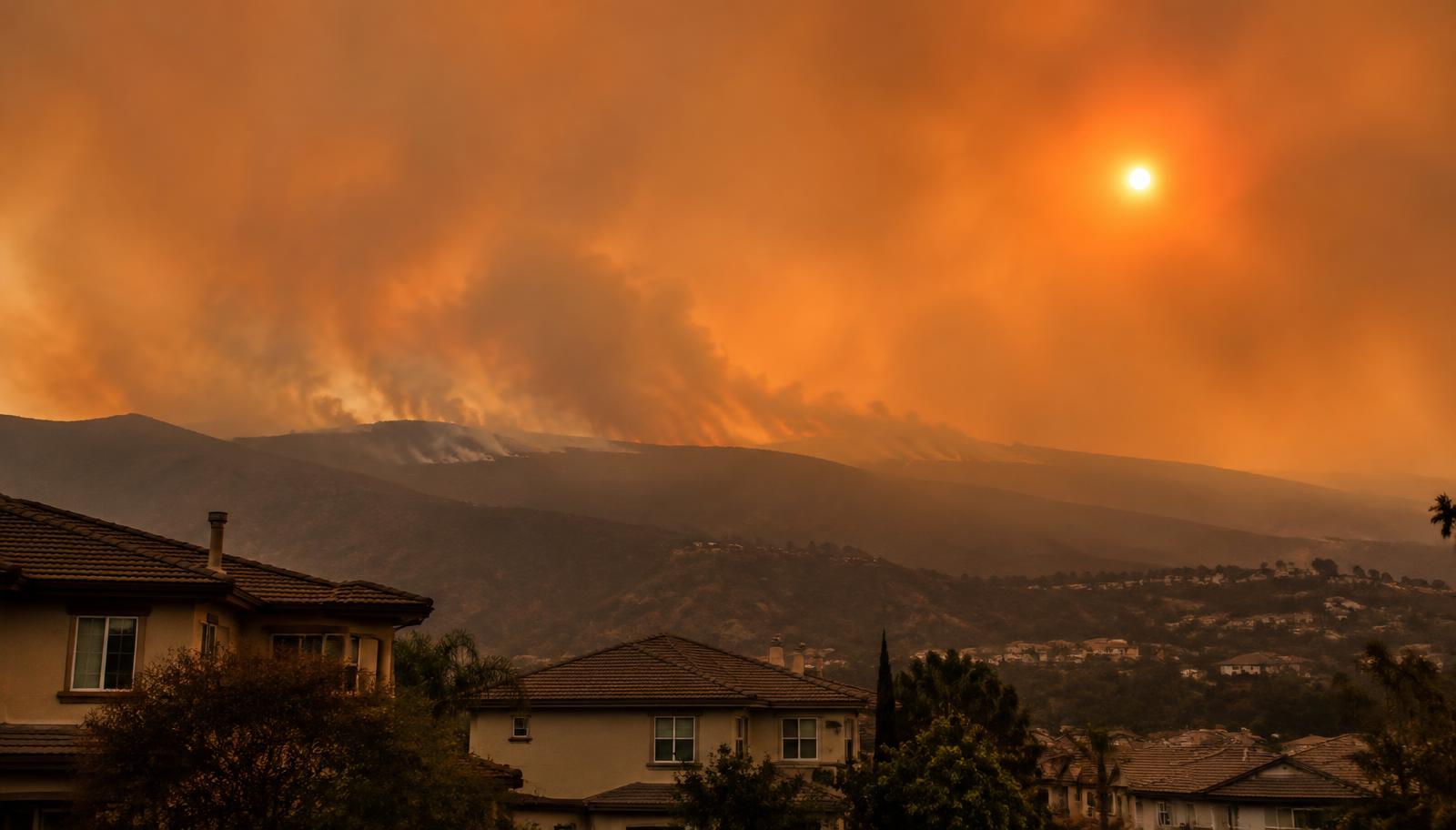 Orange wildfire smoke haze over Southern California hills behind suburban homes